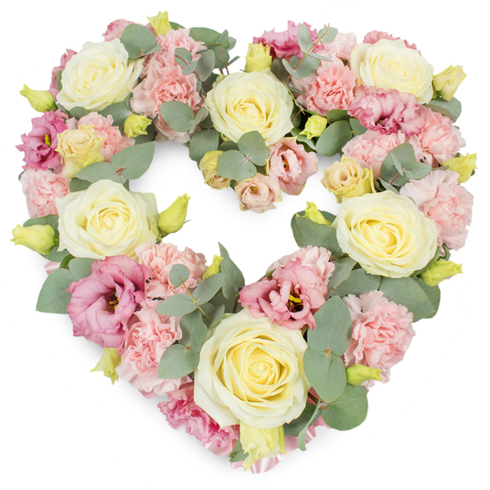 A beautifully composed heart-shaped funeral wreath is displayed against a crisp white background, allowing every detail of the design to stand out clearly. The heart itself is fully formed and symmetrical, with flowers arranged so closely that the outline appears smooth and continuous. Cream and soft yellow roses provide the main structure of the piece, their rich, velvety petals spiralling from compact centres into generous, open blooms that speak of devotion and respect. Threaded between these roses are clusters of light pink carnations, each bloom made up of numerous ruffled petals that lend volume and a soft, cushion-like texture. Scattered throughout are deeper magenta and mauve-pink lisianthus flowers, their slightly trumpet-shaped, more open petals bringing a subtle sense of movement and depth, much like the play of evening shadows along Danebury Avenue or by Roehampton Gate. Tiny yellow-green buds are sprinkled among the larger flowers, hinting at new beginnings and the freshness of the arrangement. Completing the design, sprigs of silvery-green eucalyptus weave through the heart, their rounded leaves creating a cool, calming contrast to the warm pastel tones and helping to define the elegant heart shape. The wreath is full and luxurious without feeling heavy, a carefully balanced tribute that feels both contemporary and timeless. Prepared with sensitivity by a local Roehampton florist, this heart-shaped arrangement is ideal for funerals, memorial services, or anniversary remembrances, conveying love, sympathy, and the enduring bond shared with someone dearly missed.