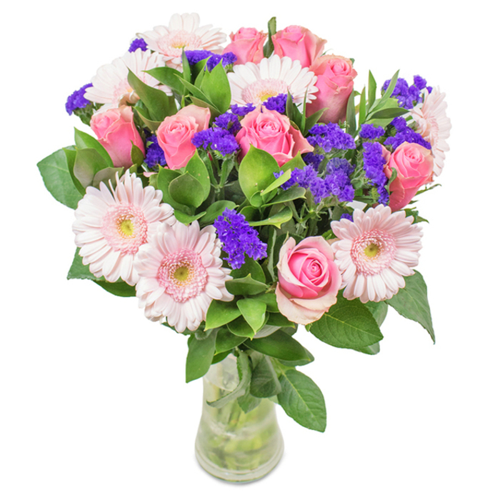 Presented in a crystal-clear glass vase and illuminated against a pristine white backdrop, this artful bouquet harmonizes approximately 7-9 mid-pink roses-each displaying classic spiral arrangements and gently opening petals-with around 5-7 pale pink gerbera daisies. The daisies are distinguished by broad, rounded heads and subtle, near-white centres, complementing the roses for a visually pleasing symmetry. Scattered among the main blooms are lively clusters of vivid purple statice or limonium, delivering textural contrast and a deeper note of colour. The whole display is reinforced by a foundation of deep green, glossy foliage, evoking freshness akin to the vibrant parks surrounding Roehampton. The transparent vase showcases the sturdy green stems and pristine water, underscoring the sense of just-cut freshness-perfect for a thoughtful gift or a new accent for a South-West London flat. This arrangement, brimming with roses, gerbera daisies, and purple fillers, suits birthdays, anniversaries, Mother's Day, or a brightening touch for home or office, conveying celebration and heartfelt affection.